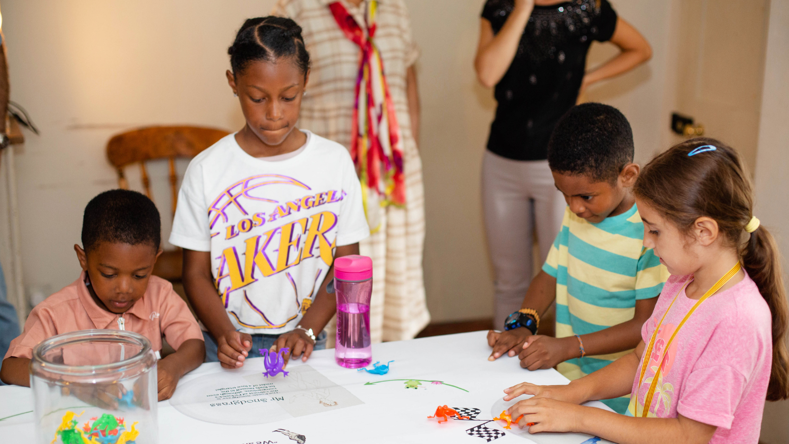 A small group of children playing a museum activity, racing toy frogs across a table. 